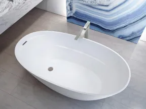 Modern white freestanding oval bathtub with sleek faucet on gray tile floor and blue marble wall art.