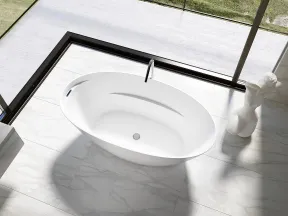Modern white freestanding bathtub on marble floor with ocean view through glass walls and sculpture nearby