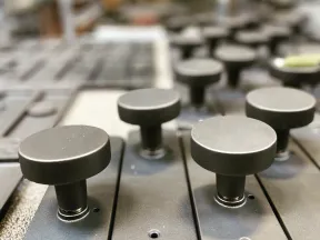 Close-up of multiple black round control knobs on matte rectangular plates arranged in rows on a textured surface.