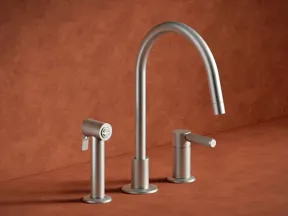 Brushed stainless steel modern kitchen faucet with side sprayer and single lever on a rust-colored countertop.