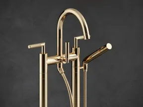 Modern gold freestanding bathtub faucet with handheld shower against dark gray background