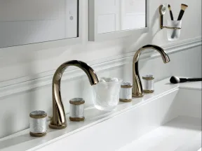 Modern double bathroom sink with sleek gold faucets, decorative jars, a white towel, and makeup brushes.