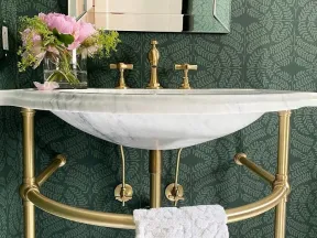 Elegant bathroom sink with brass fixtures, marble countertop, green leaf-patterned wallpaper, and pink flowers in vase.