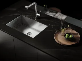 Modern kitchen sink with sleek stainless steel basin and dark marble countertop featuring a wooden tray with glassware and green olives.