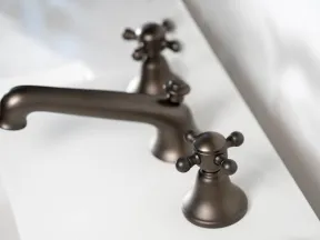 Close-up of a matte black faucet and dual handles on a white bathroom sink countertop.