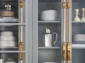 Gray kitchen cabinet with textured glass doors displaying white dishes, pitchers, and gold hardware handles.