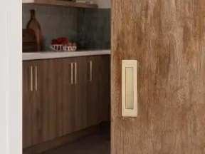 Sliding wooden door with recessed handle partially open to reveal modern kitchen with wooden cabinets and countertop.