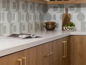 Modern kitchen corner with wooden cabinets, white countertop, geometric backsplash tiles, and open shelves.