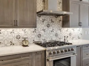 Modern kitchen with gray wood cabinets, stainless steel gas stove, and floral patterned tile backsplash.