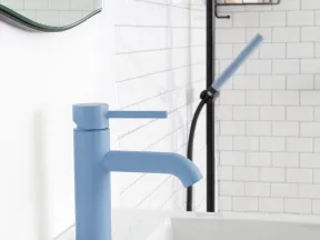 Matte blue bathroom faucet installed on white countertop with white subway tile wall and black shower fixture in background