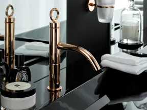 Modern bathroom sink with rose gold faucet, black countertop, toiletries, and white towels neatly arranged.