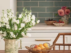 Rustic kitchen table with fresh flowers, fruit bowls, ceramic plates, and vintage kitchen decor.