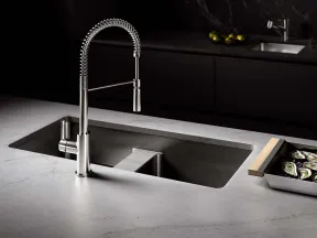 Modern kitchen sink with a sleek stainless steel spring coil faucet on a marble countertop with oysters on a tray.