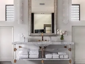 Elegant bathroom with a large arched mirror, marble countertop, clear vanity, and neatly stacked white towels.