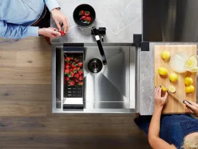 Top view of two people preparing strawberries and lemons on a kitchen counter with a modern stainless steel sink.