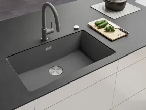 Modern kitchen sink with matte black faucet on dark countertop, cutting board with zucchini, and pot in background