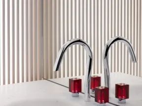 Modern bathroom sink with chrome faucet and red square handles against a striped beige wall and mirror.