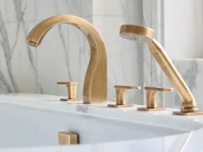 Modern bathroom with gold-tone faucet and hand shower set against white marble backdrop