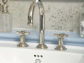 Chrome bathroom faucet with cross handles above white sink and decorative glass containers on sides