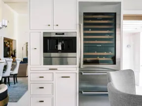 Modern kitchen cabinetry with built-in coffee machine and stainless steel wine fridge beside seating area.