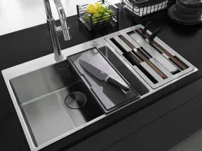 Modern kitchen sink with chrome faucet, integrated cutting board, and organized knife storage on black countertop