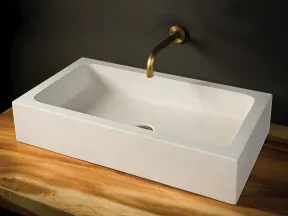Modern rectangular white bathroom sink with brass wall-mounted faucet on wooden countertop