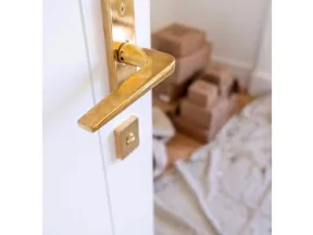 Close-up of a gold door handle on a white door with stacked cardboard boxes and a drop cloth in the background