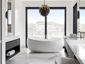 Modern bathroom with freestanding white tub, marble flooring, black cabinetry, large window, and stylish pendant light.