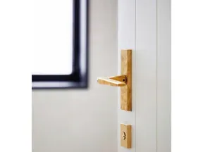 Close-up of modern gold door handle and lock on a white door near a window with soft natural light.