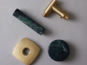 Brass faucet parts and green marble accessories displayed on a textured gray surface.