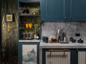 Blue kitchen cabinets with marble countertops, decorative nature mural, wooden flooring, and glassware display.