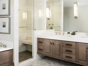 Modern bathroom with wooden vanity, large mirror, glass shower enclosure, geometric tile floor, and wall art.