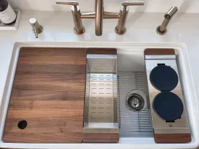 Modern kitchen sink with brass faucet, removable wood covers, stainless steel drying rack, and accessories