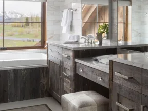 Rustic bathroom with dark wood cabinets, a cushioned vanity stool, marble countertops, and a large window with mountain view.