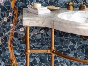 Marble bathroom sink with brass fixtures and floral mosaic tile wall in blue and pink tones.