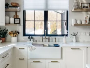 Bright modern kitchen with white cabinetry, farmhouse sink, brass fixtures, and large window overlooking snowy yard.