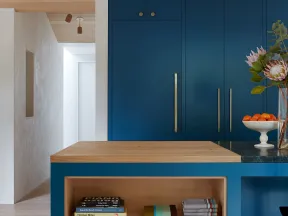 Modern kitchen island with blue cabinetry, wooden countertop, decorative vases, and books on open shelves