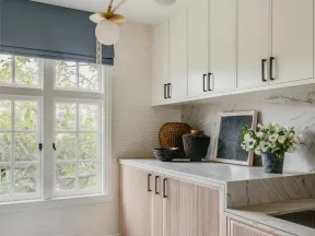 Bright kitchen corner with white and wood cabinets, marble countertop, modern light fixture, and decorative plants.