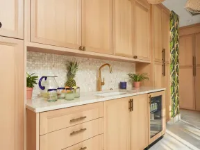 Light wood kitchen cabinets with gold faucet, mosaic tile backsplash, and tropical-themed wallpaper accent.
