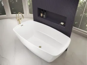 Modern white freestanding bathtub with gold faucet in bright bathroom with purple textured wall niche and large windows.