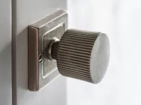 Close-up of a vintage metal door knob with ridged texture on a white wooden door.