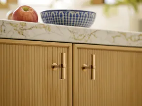 Brass cabinet handles on wood grain kitchen cabinets with marble countertop holding a red apple and blue bowl