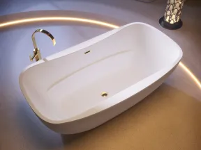Modern white freestanding bathtub with gold faucet and ambient circular floor lighting in a stylish bathroom.