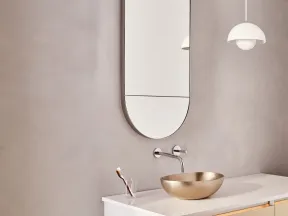 Minimalist bathroom with oval wall mirror, brass vessel sink, white floating vanity, and modern pendant light.