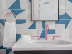 Modern bathroom sink with pink faucet and towel ring, geometric blue and white tiled wall, and wooden cabinet.