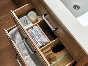 Open bathroom vanity drawers with towels, brushes, skincare jars, and grooming tools under a white sink.