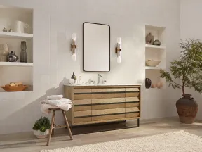 Modern bathroom with wooden vanity, rectangular wall mirror, decorative shelves, stool with towels, and large potted plant.
