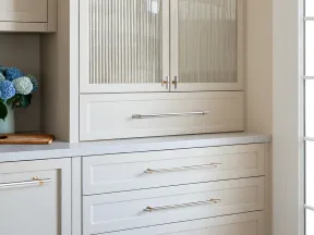 Modern white kitchen cabinets with ribbed glass doors and sleek metallic handles beside a bouquet of blue and white flowers.