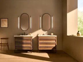 Modern bathroom with twin wooden vanities, oval mirrors, vertical lights, and natural sunlight through window.