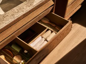 Open wooden bathroom drawer with neatly organized towels, brushes, and toiletries under a marble sink countertop.